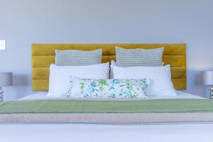 Una cama bien tendida con un plaid verde, un cabecero amarillo y dos lámparas de noche.