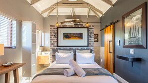 A well-lit bedroom with a bed, a wooden table, a built-in wardrobe, and a large framed picture on the wall. - Boardwalk Lodge - B&B (Wilderness)