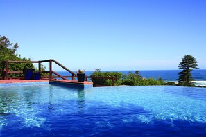 A infinity pool with a wooden deck and potted plants, overlooking a beach and ocean. - Boardwalk Lodge - B&B (Wilderness)