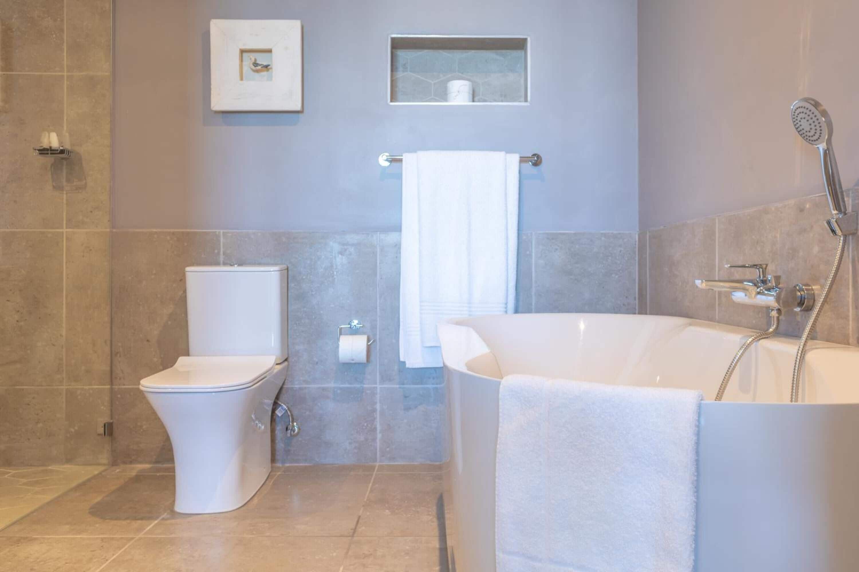 Un baño moderno con inodoro, bidé y bañera, que incluye un perchero y un cuadro en la pared.