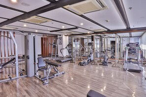Un gimnasio con varios equipos de ejercicio, suelo de madera y un muro con espejos.