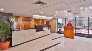 A hotel reception area with a reception desk, a wooden wall with the hotel name, a large potted plant, and a modern chandelier. - Avari Xpress Multan (Multan)
