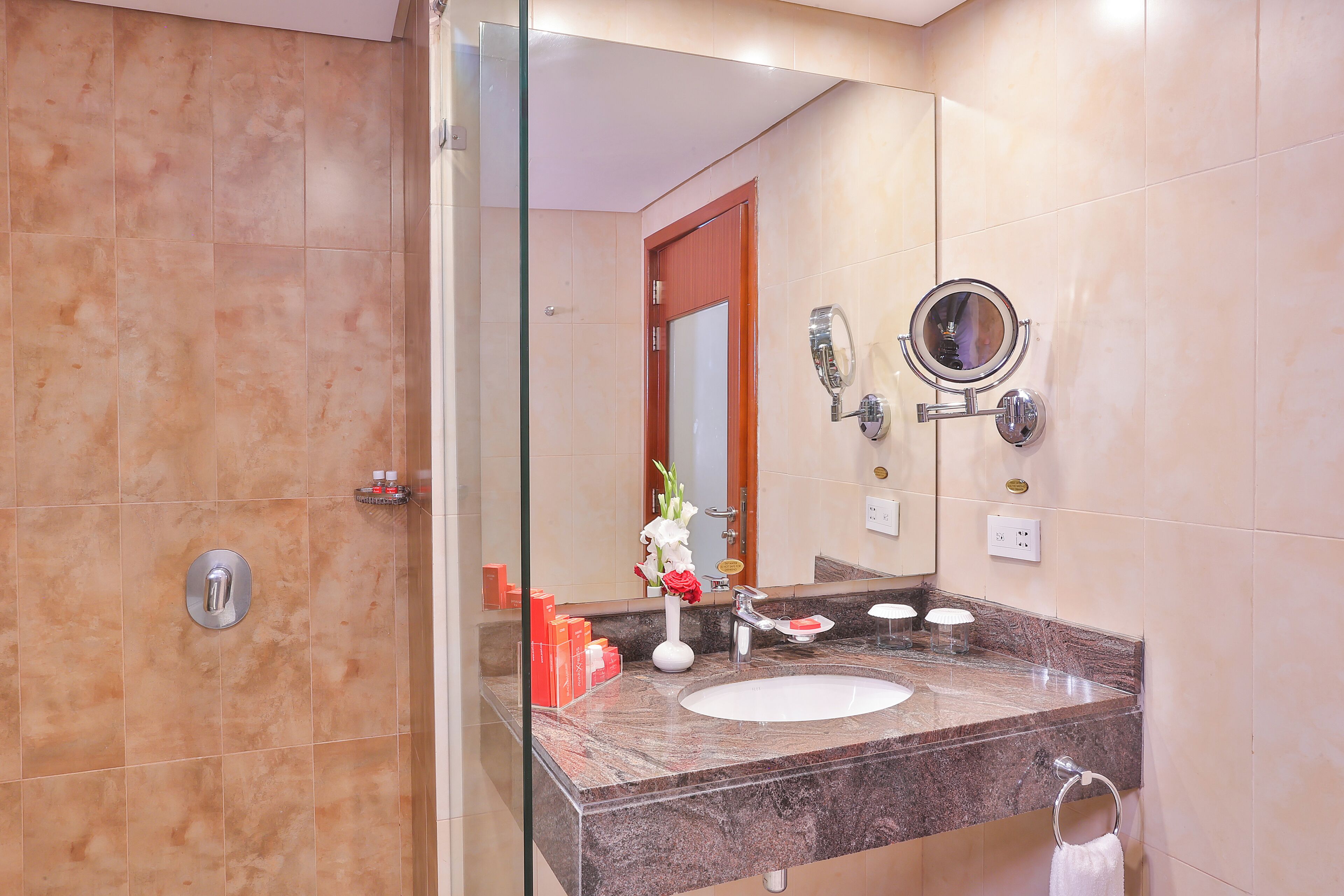 A bathroom with a marble sink, a mirror, a glass shower enclosure, and a towel ring.