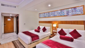 A hotel room with two beds, a wooden door, a patterned wall decoration, and a nightstand with a lamp. - Avari Xpress Multan (Multan)