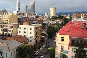 Paisagem urbana com diversos edifícios, incluindo estruturas residenciais e comerciais, e uma rua movimentada com carros.