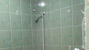 Casa de banho com paredes azulejadas em verde, chuveiro com um chuveiro manual e lavatório pedestal branco.
