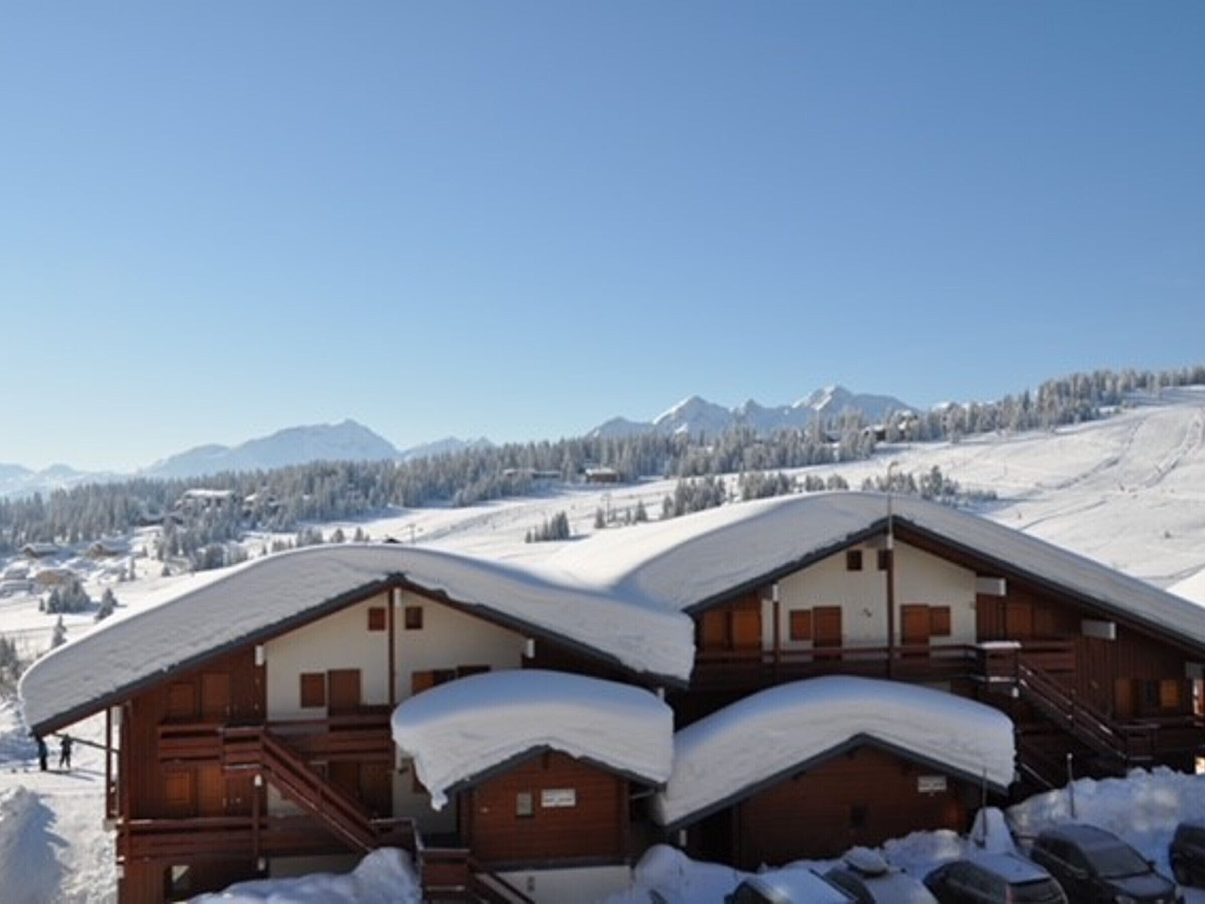 A wooden lodge with a sloped roof, surrounded by snow-covered mountains and trees.