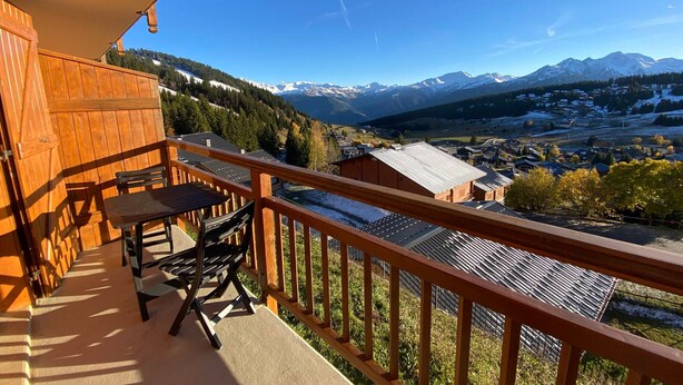 A wooden balcony with a table and chairs, overlooking a mountainous landscape with a village below. - Charming 2-room apartment, 4 pers, sunny view in Les Saisies (Les Saisies)