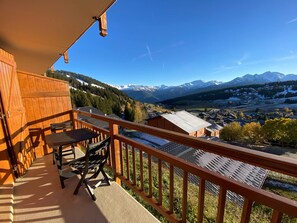 A wooden balcony with a table and chairs, overlooking a mountainous landscape with a village below. - Charming 2-room apartment, 4 pers, sunny view in Les Saisies (Les Saisies)