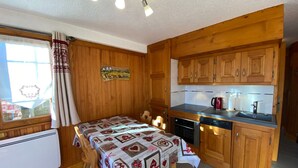 A cozy kitchen with wooden cabinets, a dining table with a festive tablecloth, and a window with curtains. - Charming 2-room apartment, 4 pers, sunny view in Les Saisies (Les Saisies)