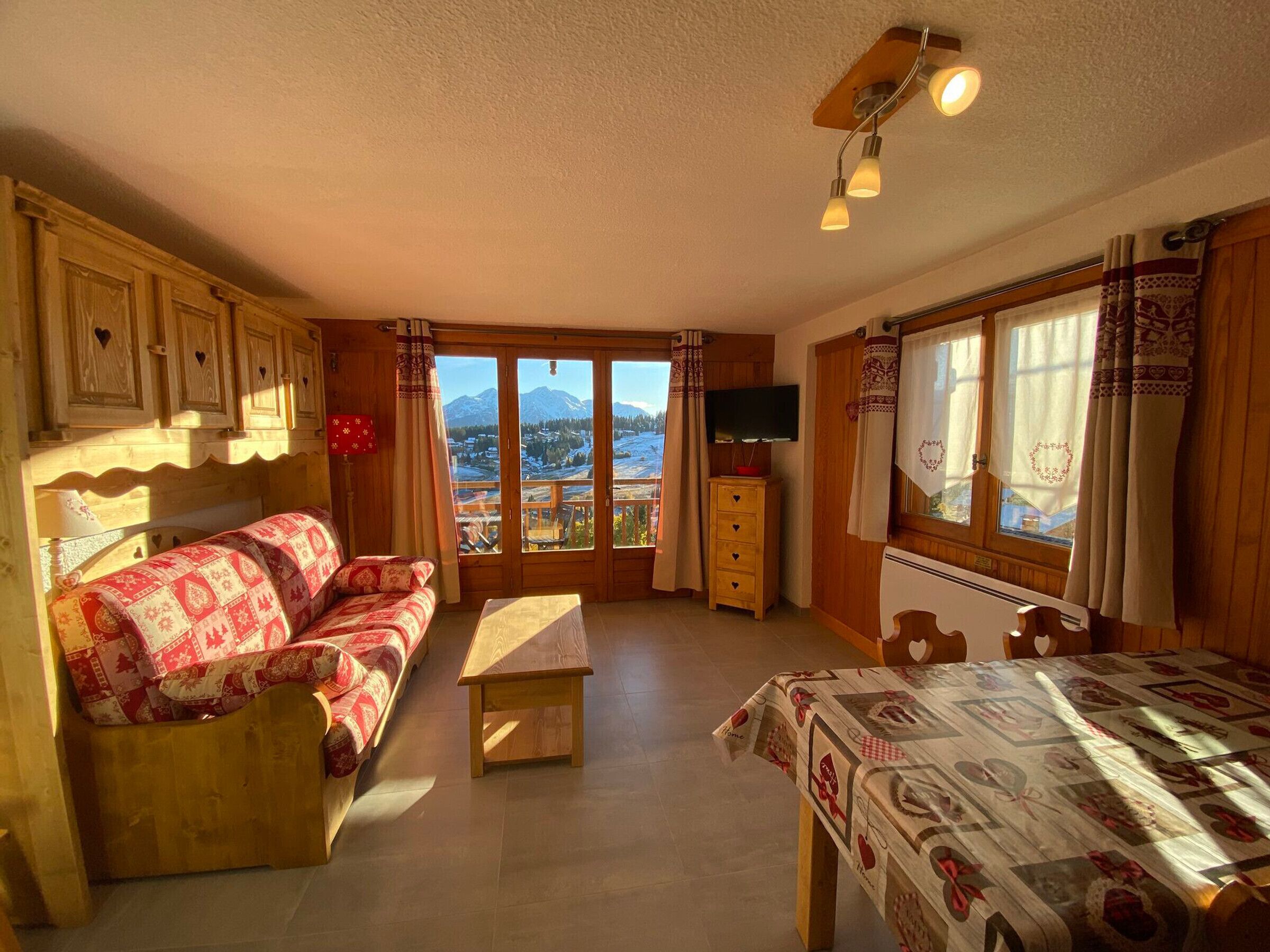 A cozy room with a wooden sofa, a small table, a TV, and a window with a mountain view.