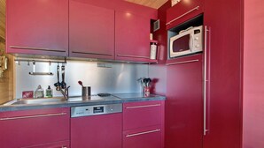 A modern kitchen with red cabinets, stainless steel appliances, and a wooden ceiling. - Family apartment near slopes (La Plagne)