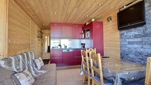 A cozy cabin interior with a wooden ceiling, a red kitchen, a dining area with a table and chairs, and a flat-screen TV mounted on the wall. - Family apartment near slopes (La Plagne)