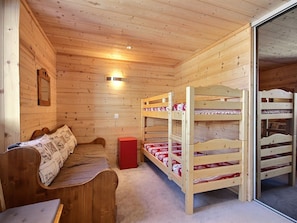 Quarto de cabana de madeira com beliches, um banco e um pequeno armário vermelho.