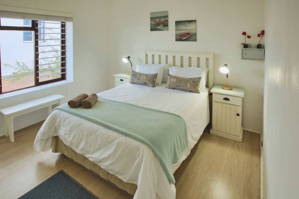 A neatly arranged bedroom with a bed, two bedside tables, a bench, and a window with blinds.