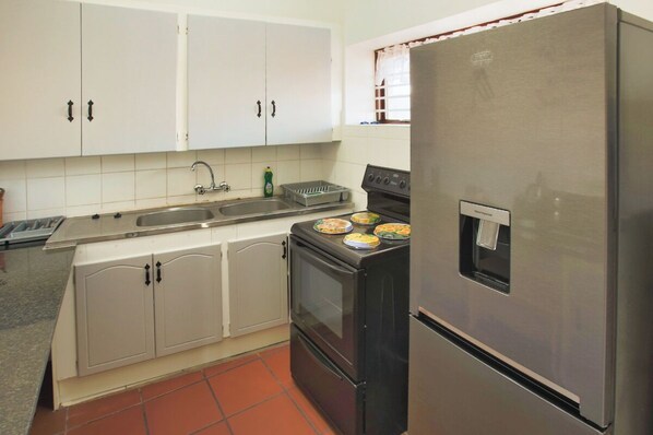 Una cocina con armarios blancos, un refrigerador de acero inoxidable, una estufa y un lavamanos.