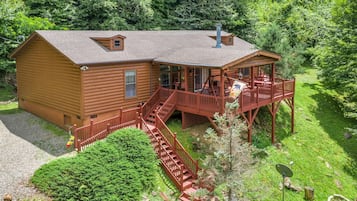 A log cabin with a two-story deck, a chimney, and a gravel driveway.