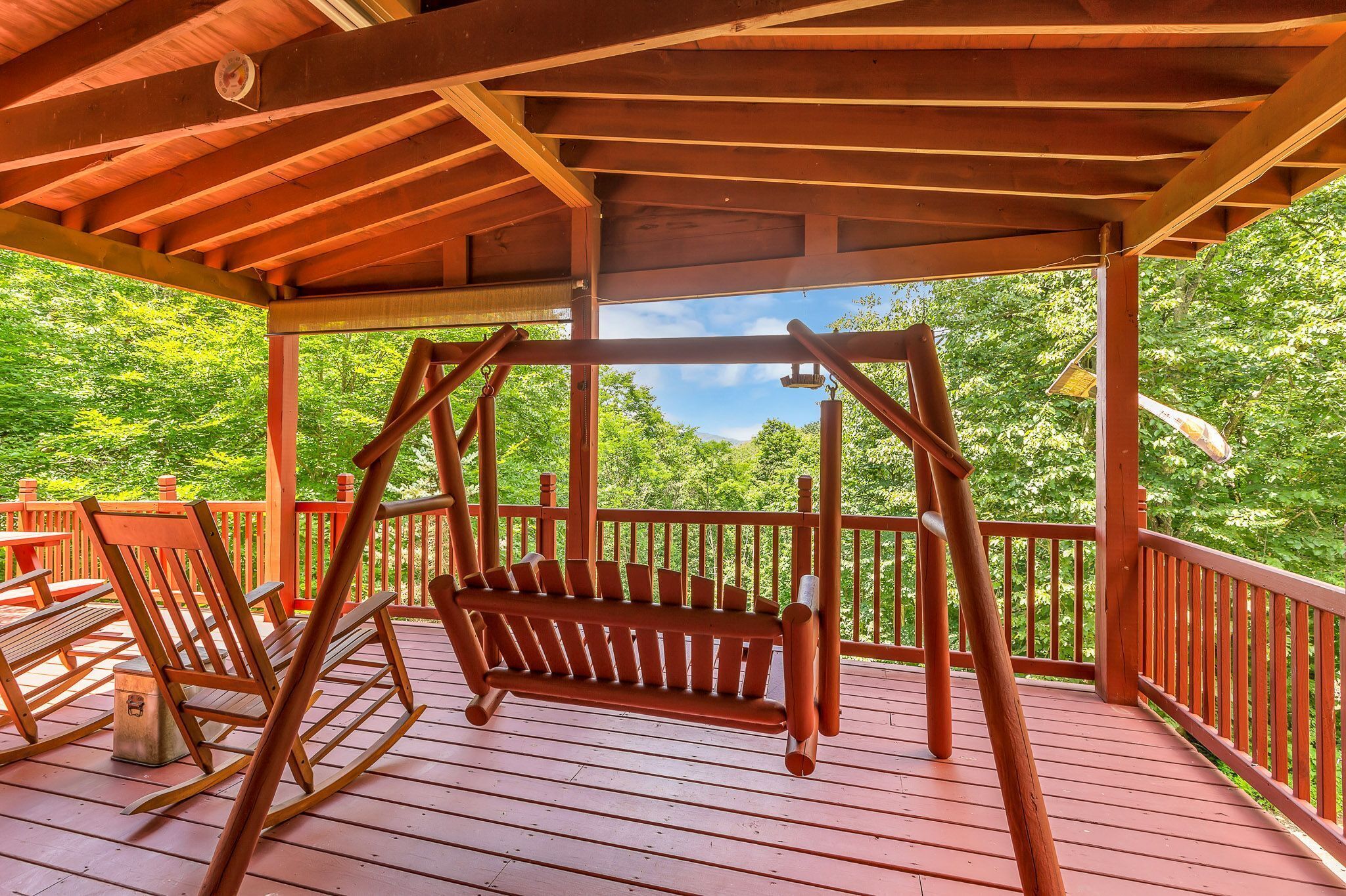 Une terrasse en bois agrémentée d’une balançoire et de fauteuils à bascule, entourée d’une rambarde en bois et d’une végétation luxuriante.