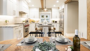 A modern kitchen with white cabinets, a wooden dining table set for two, and a bottle of wine on the table. - Walk to Trails & Main St, 4BR Hot Tub Home (Park City)