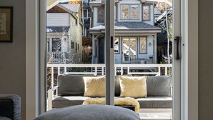 A view through a glass door to a balcony with a sofa and cushions, overlooking a residential area with houses and a tree. - Walk to Trails & Main St, 4BR Hot Tub Home (Park City)