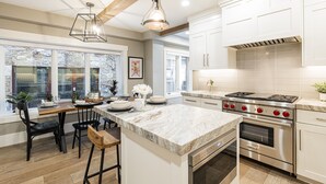 A modern kitchen with white cabinetry, a large island with a marble countertop, and a built-in oven. - Walk to Trails & Main St, 4BR Hot Tub Home (Park City)