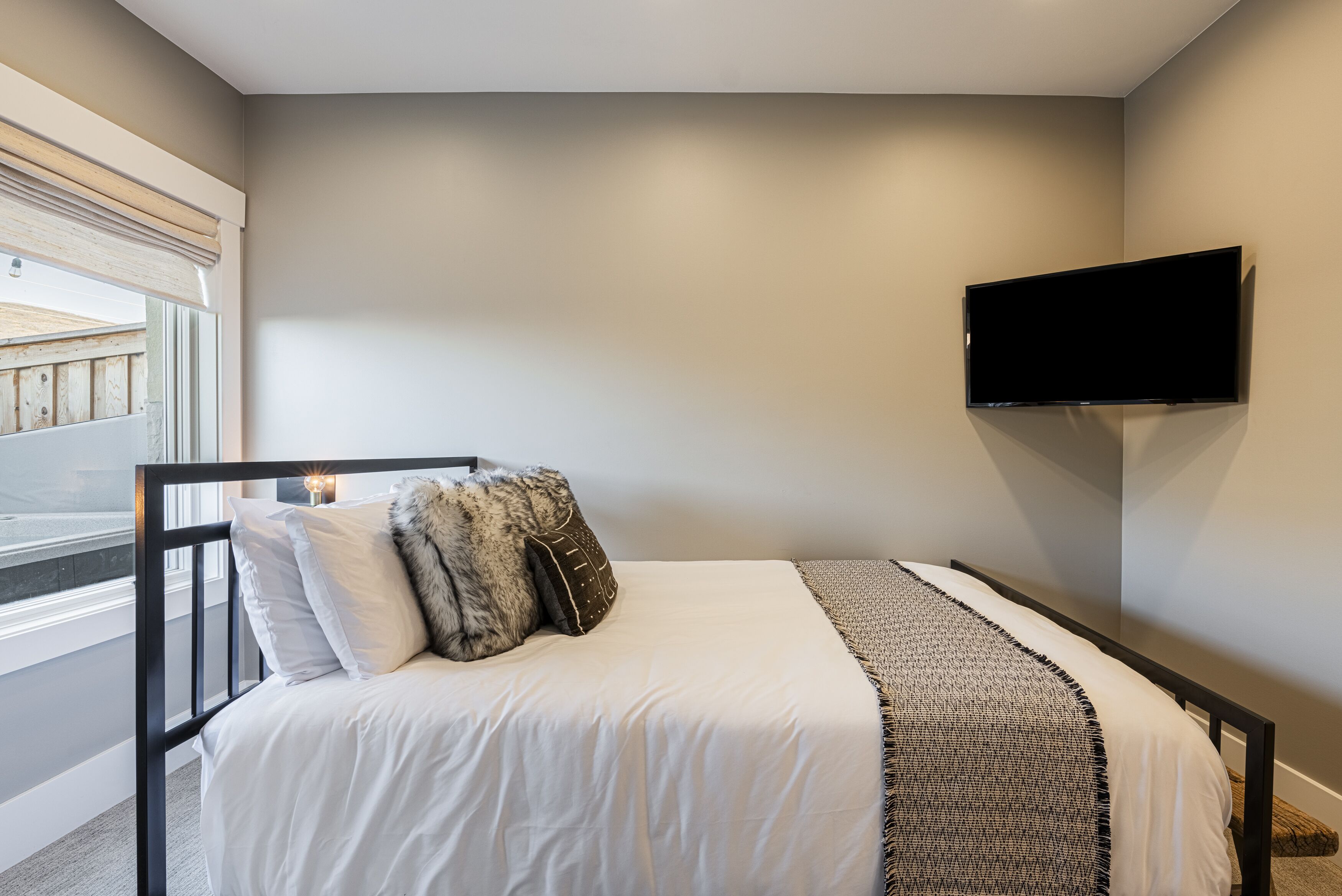 A bedroom with a bed, a TV mounted on the wall, and a window with a view of a balcony.