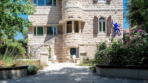 A stone building with a modern glass structure behind it, a staircase, and a statue in the foreground. - The Schumacher Hotel Haifa (Haifa)