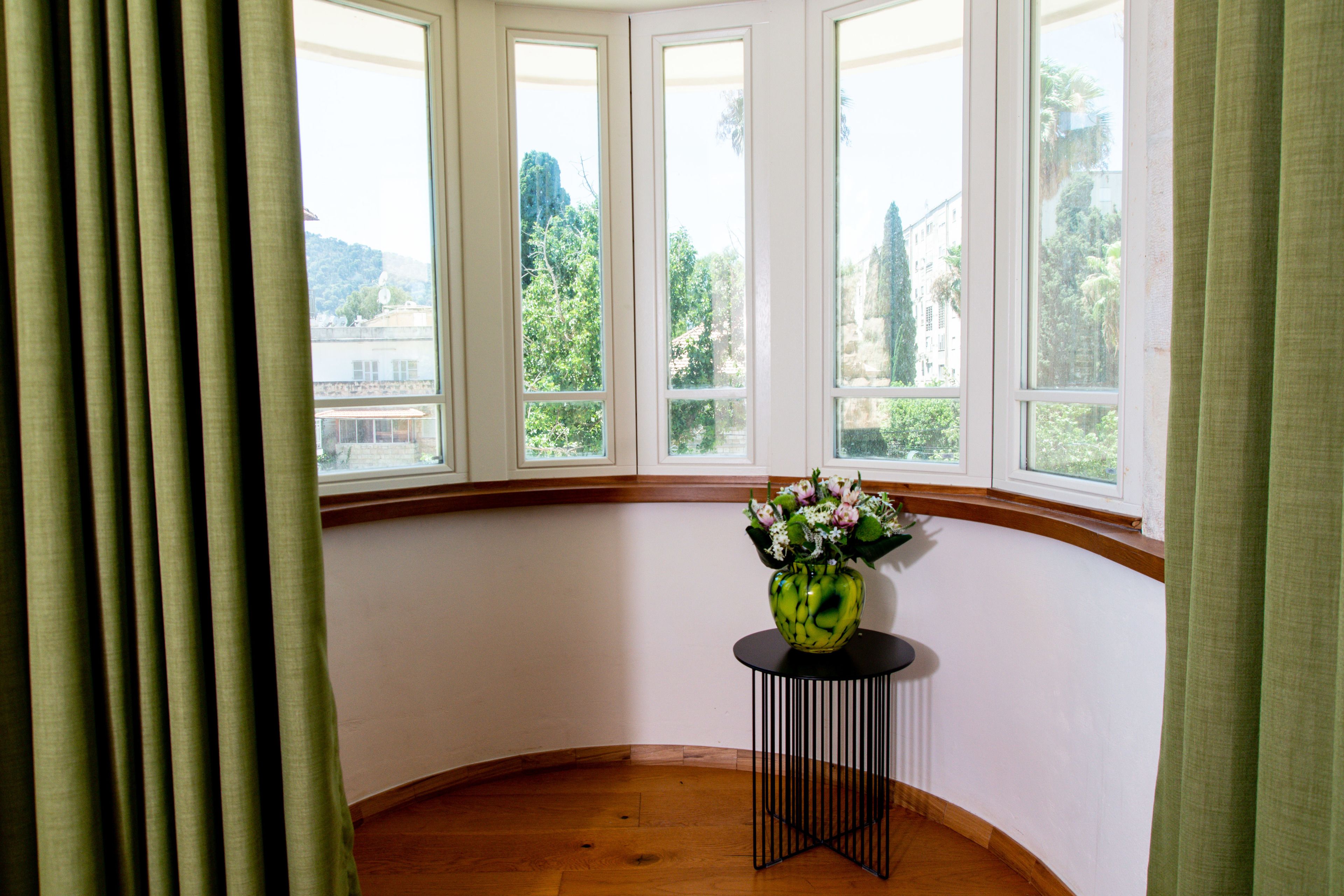 Una habitación con ventanal panorámico, una pequeña mesa con un florero y suelo de madera.