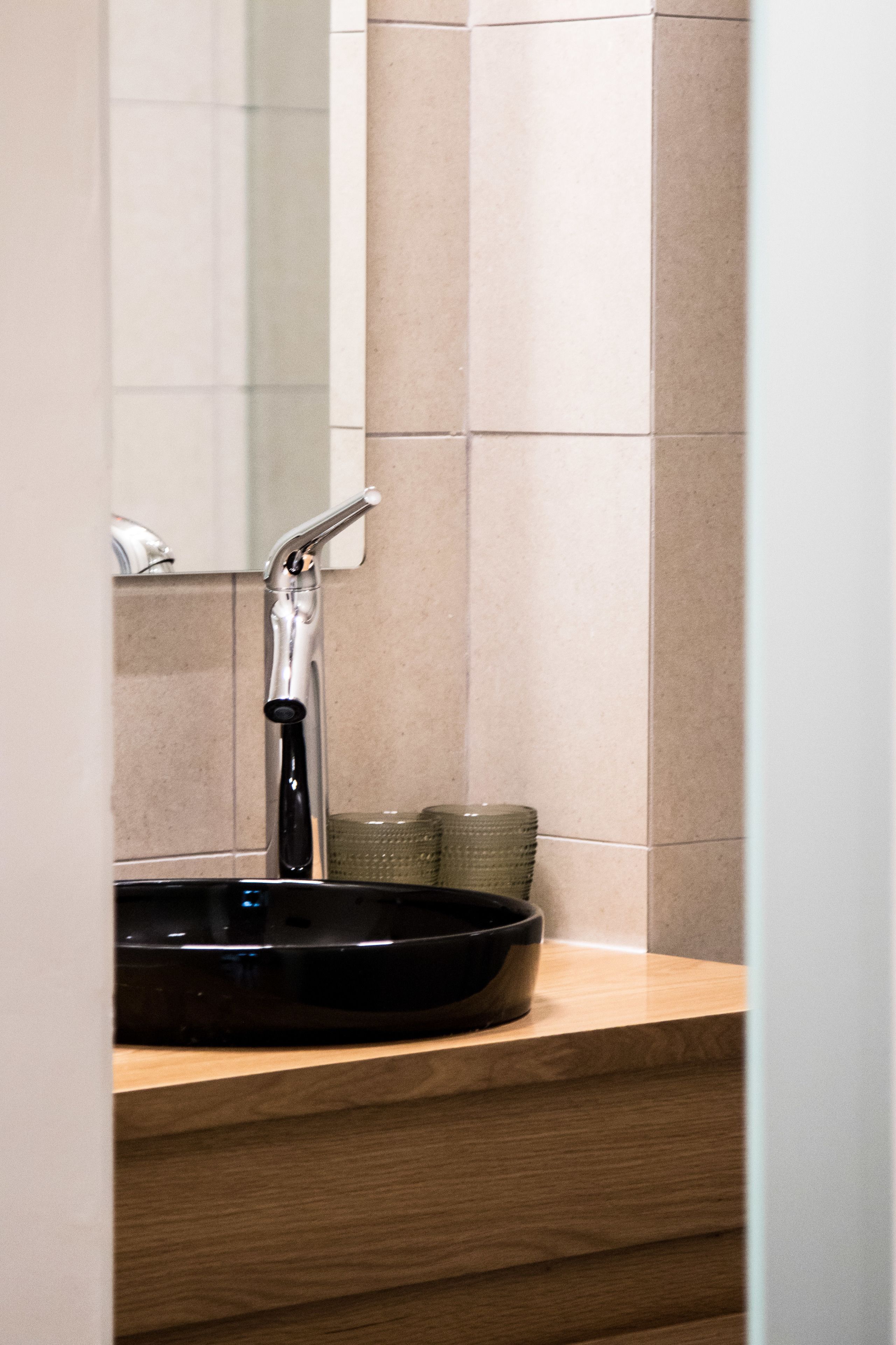 A bathroom with a modern sink, a mirror, and beige tiles.