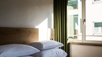 A hotel room with a wooden headboard, a bed with white bedding, a window with green curtains, and a view of a building outside.
