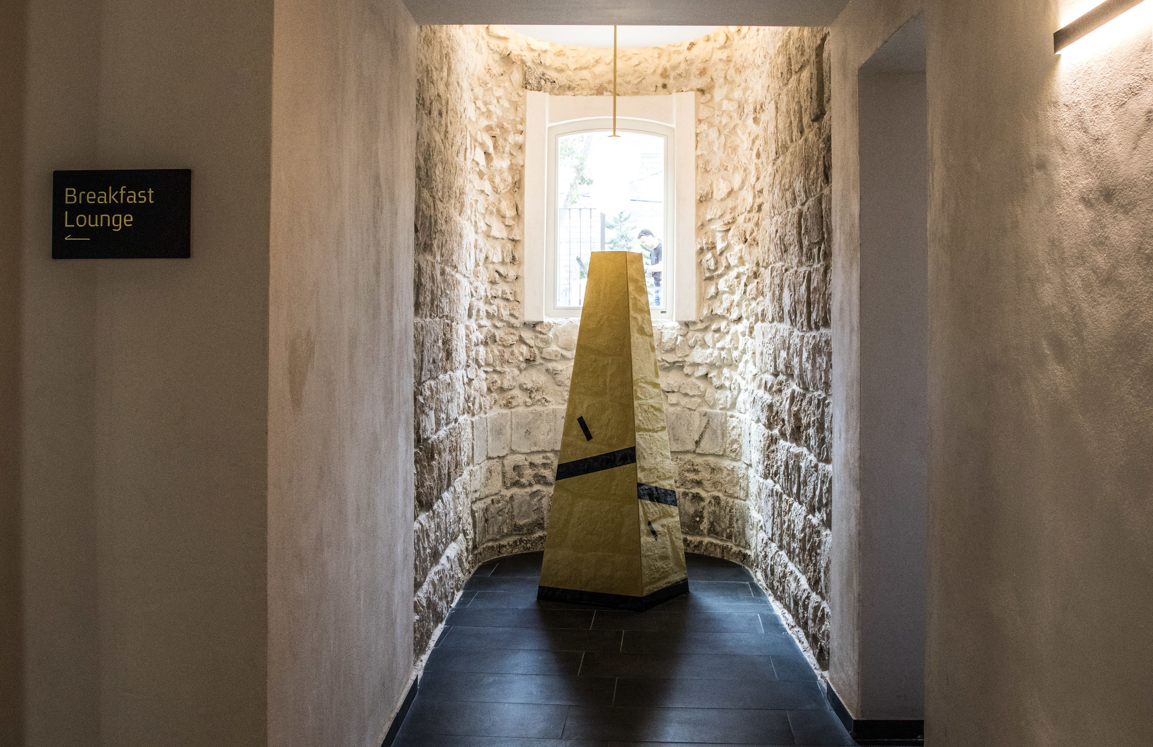 Un couloir étroit aux murs de pierre mène à une fenêtre, et une pancarte indique l’emplacement du salon où le petit-déjeuner est servi.