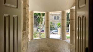 An open doorway leading to a covered outdoor area with stone columns and a view of a building in the background. - The Schumacher Hotel Haifa (Haifa)