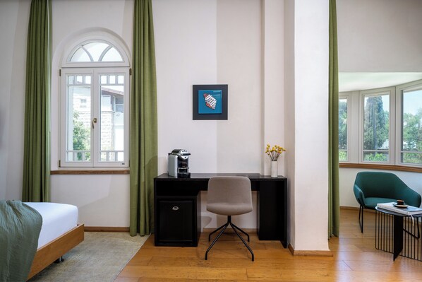 A room with a bed, desk, chair, and a small table with a book and a cup.
