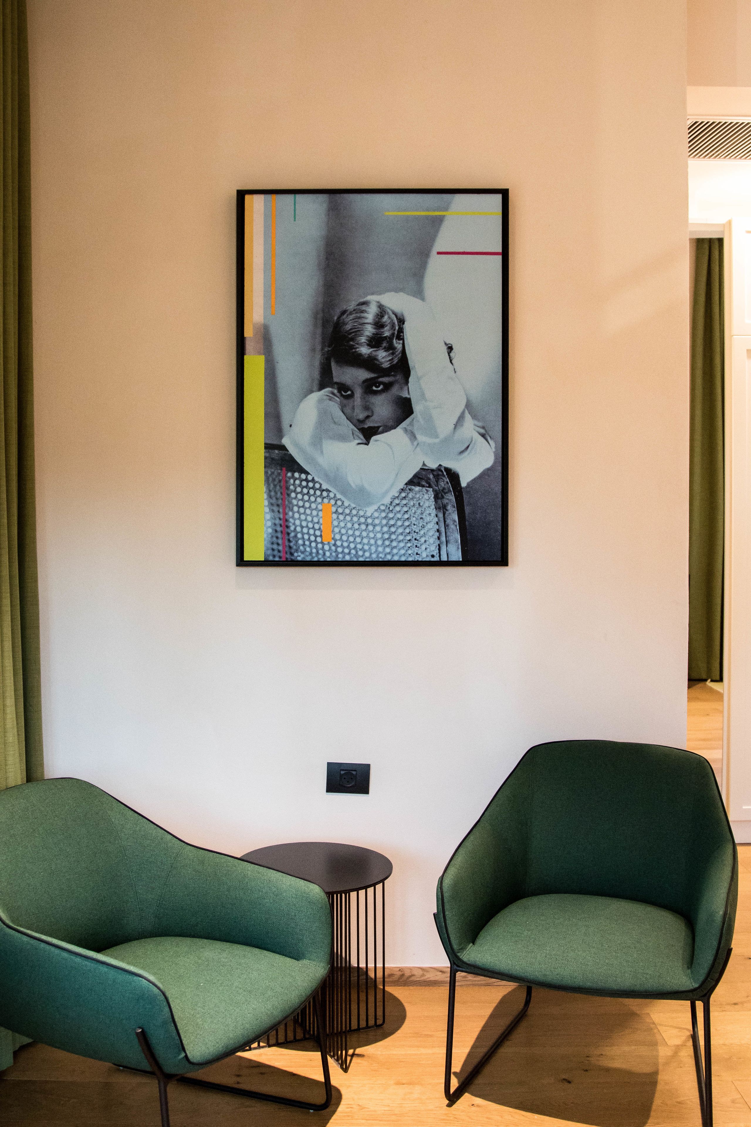 A room with two green armchairs, a framed black and white photograph on the wall, and a small round table.