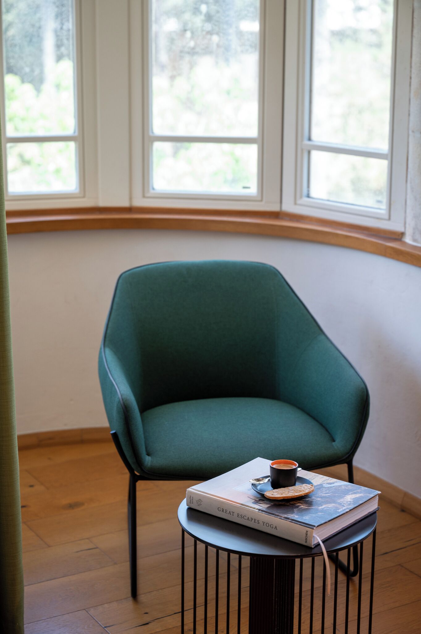 A green armchair next to a small round table with a book and a cup.