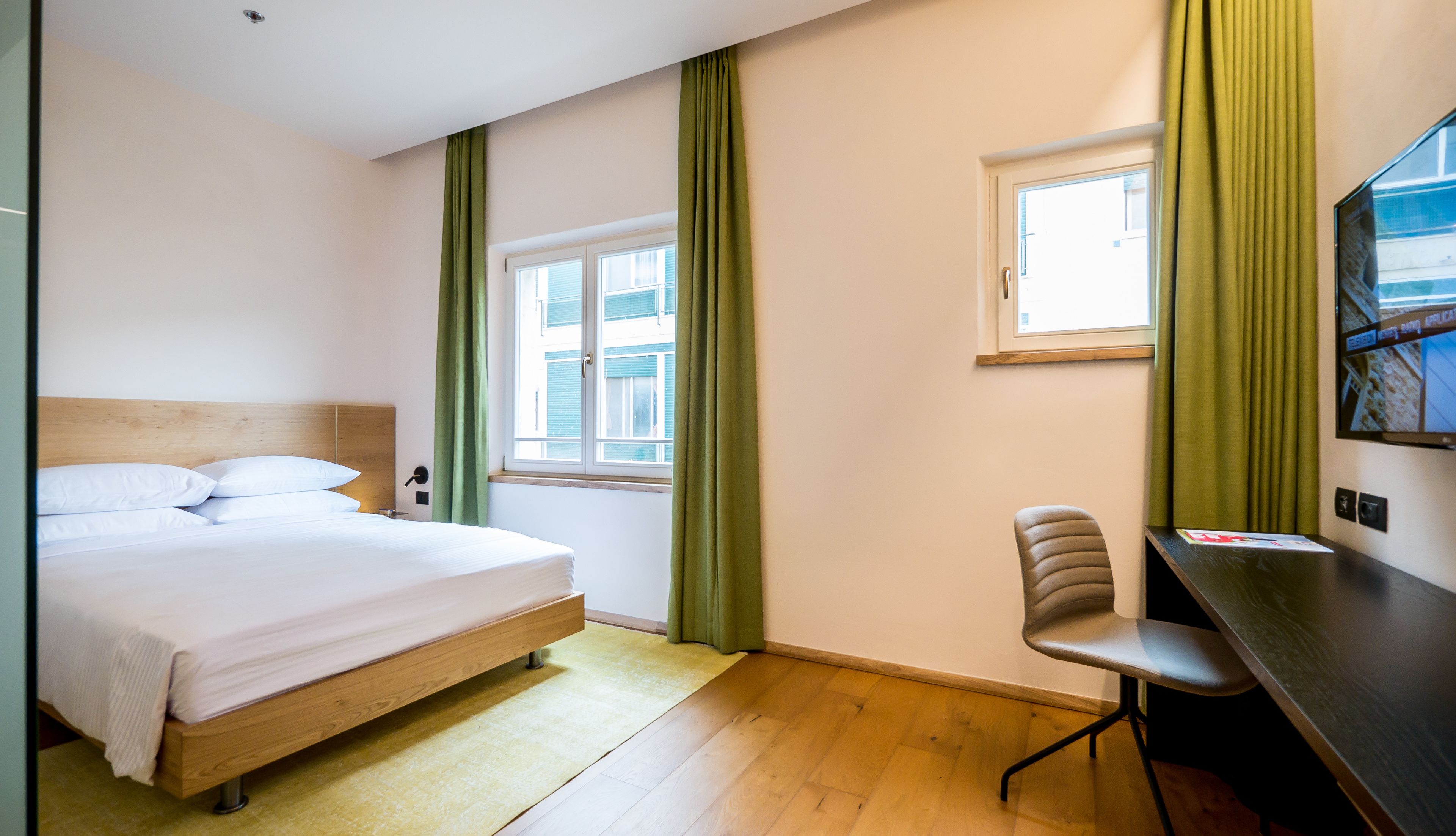 A hotel room with a bed, a desk, a chair, a window, and a television.