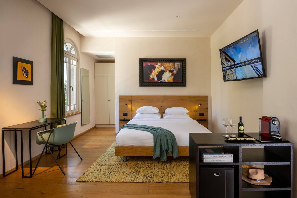 A modern hotel room with a wooden bed, a desk, a chair, a television, and a bookshelf.