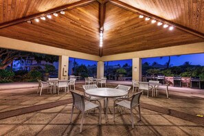 Un patio al aire libre con mesas y sillas redondas, techo de madera y vista del cielo nocturno.