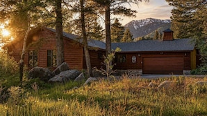 A log cabin with a garage, surrounded by trees and a mountainous backdrop. - RMR: Three Bear Tracks Home in Teton Village (Teton Village)
