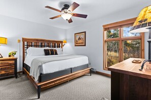 A bedroom with a wooden bed, a ceiling fan, a window with a view, and a bedside table with a lamp.
