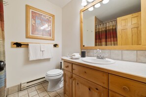 Ein Badezimmer mit Toilette, Holzschränken, einem Waschbecken und einem beleuchteten Spiegel.