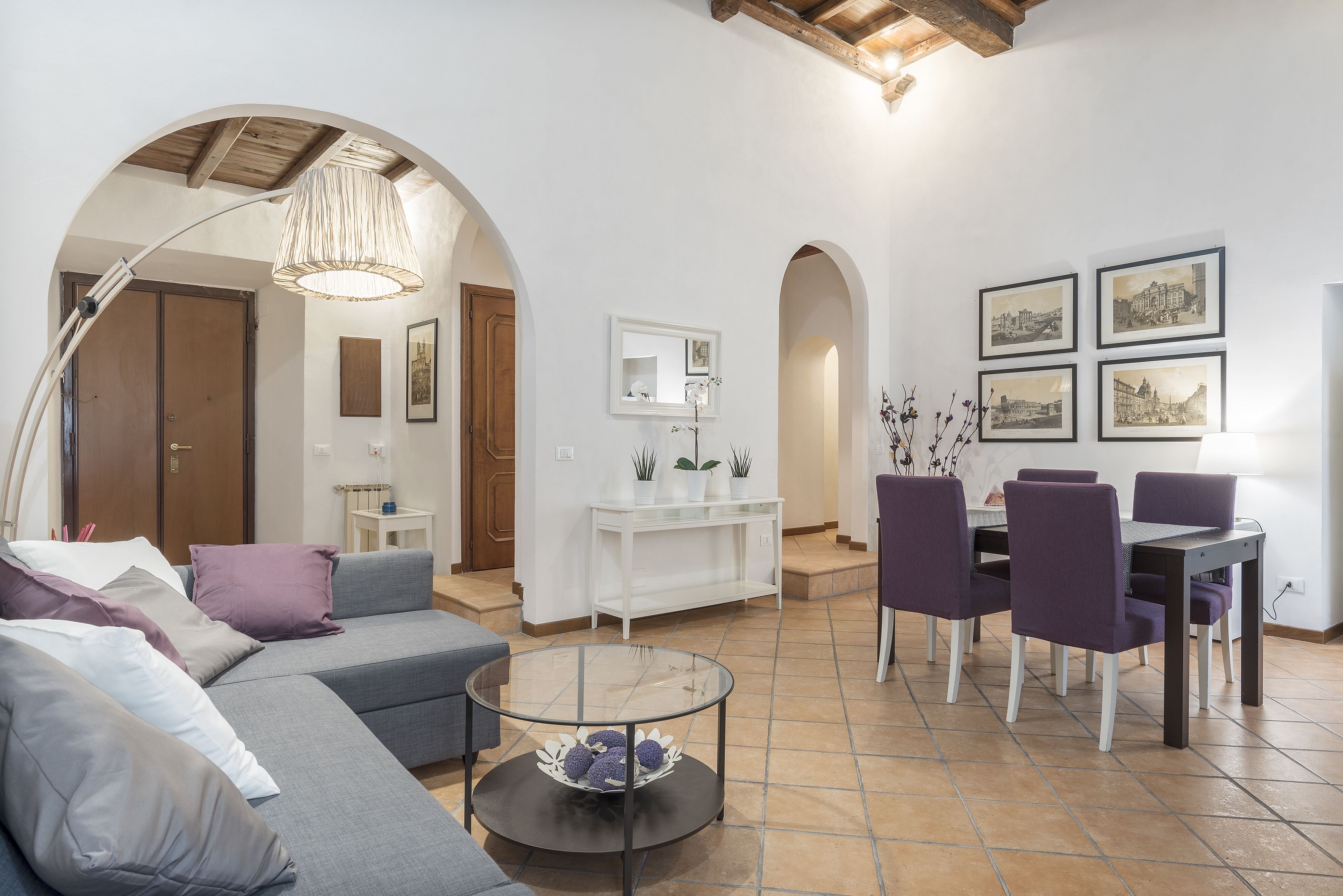 A living room with a gray sofa, purple chairs, a glass coffee table, and a white console table with plants.