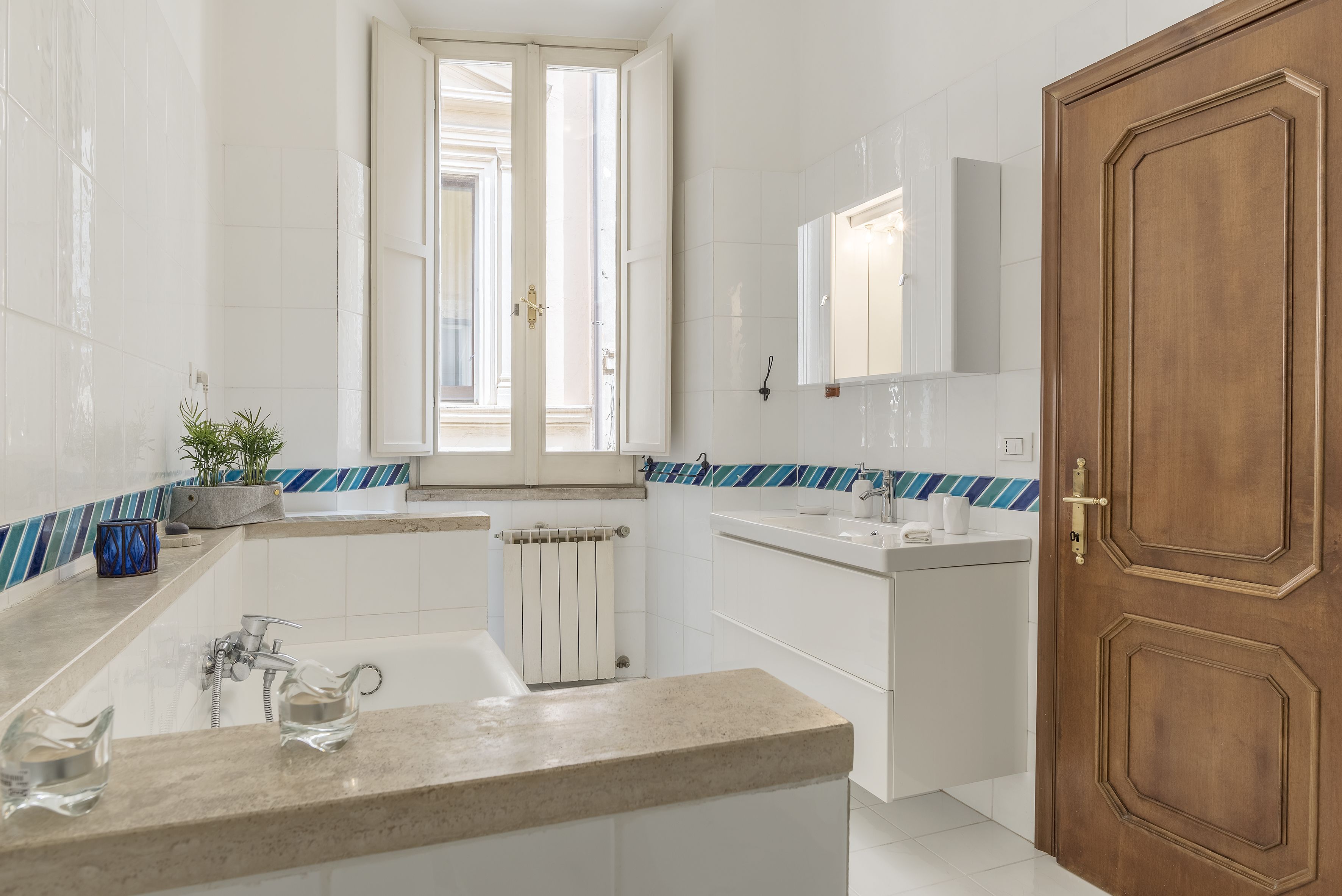 Une salle de bain moderne avec une baignoire, un lavabo et des toilettes. Il y a une fenêtre donnant sur l’extérieur et une porte en bois.