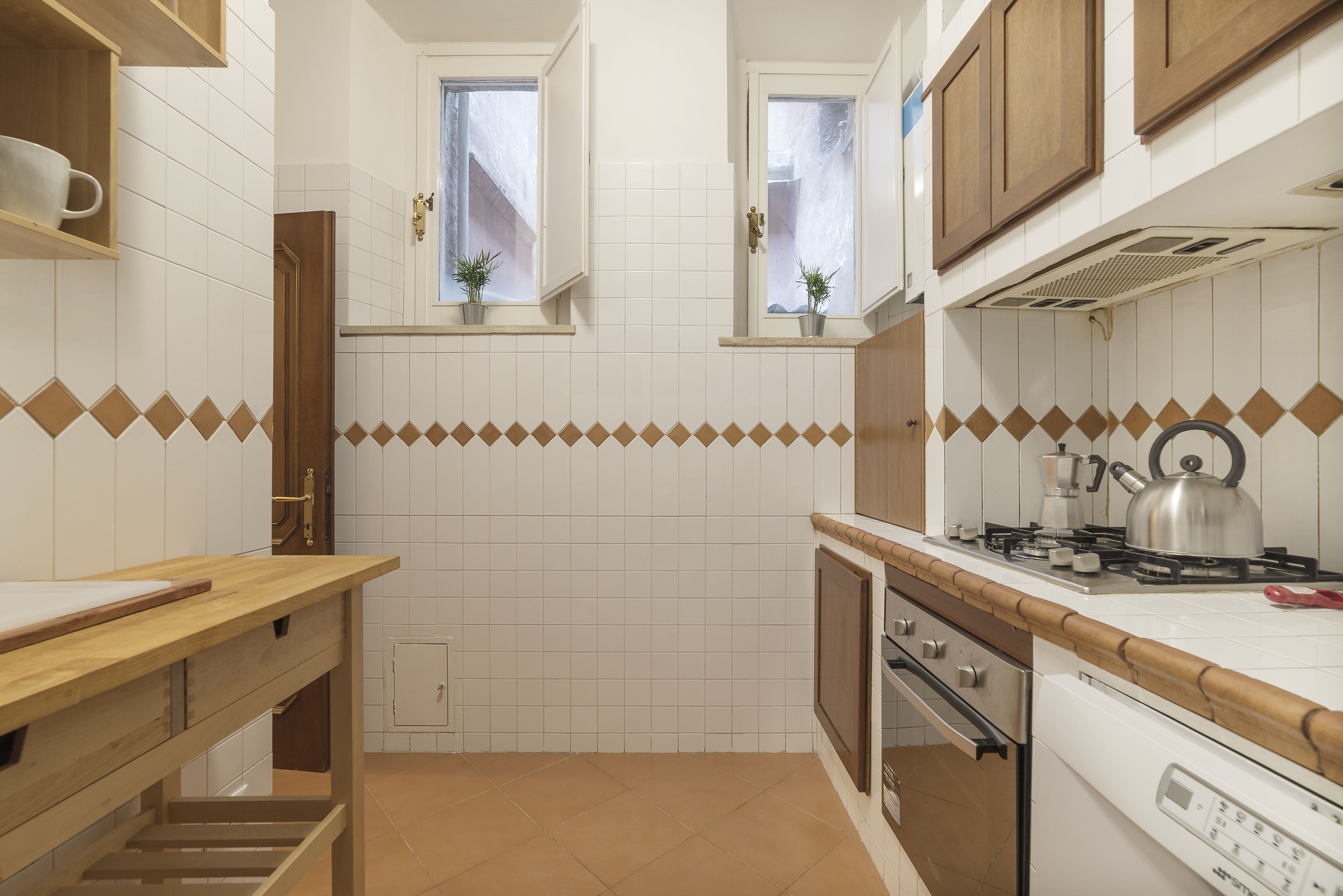 A kitchen with white tiles, wooden cabinets, a wooden countertop, and a stove.