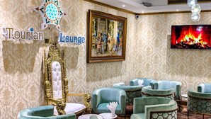 Un espace détente avec des fauteuils recouverts d’un tissu turquoise, un fauteuil doré orné, une cheminée et un tableau encadré accroché au mur.
