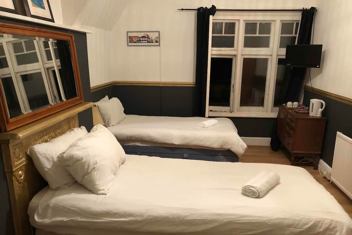 A hotel room with two single beds, a wooden dresser, a television, and a window with curtains.