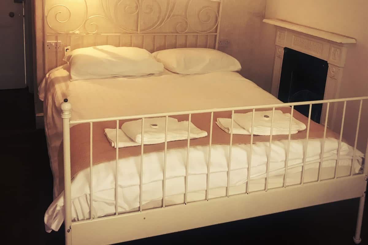 A neatly made bed with white linens, a white metal headboard, and a white wall with two framed pictures.