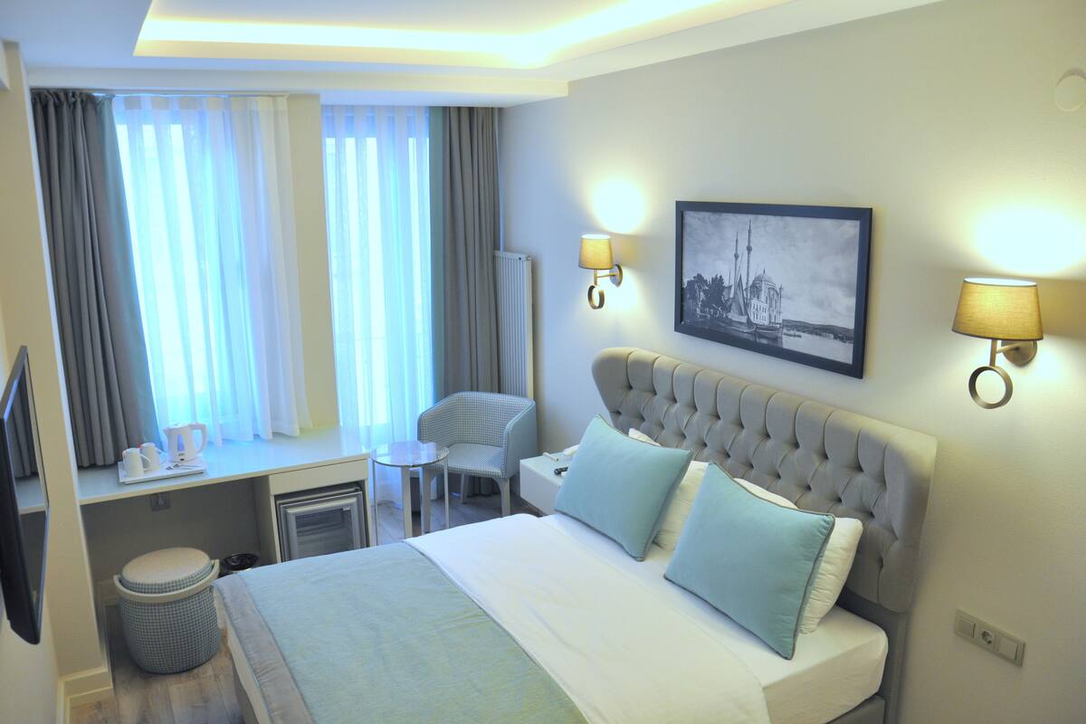 A hotel room with a bed, a desk, a chair, and a window with curtains.