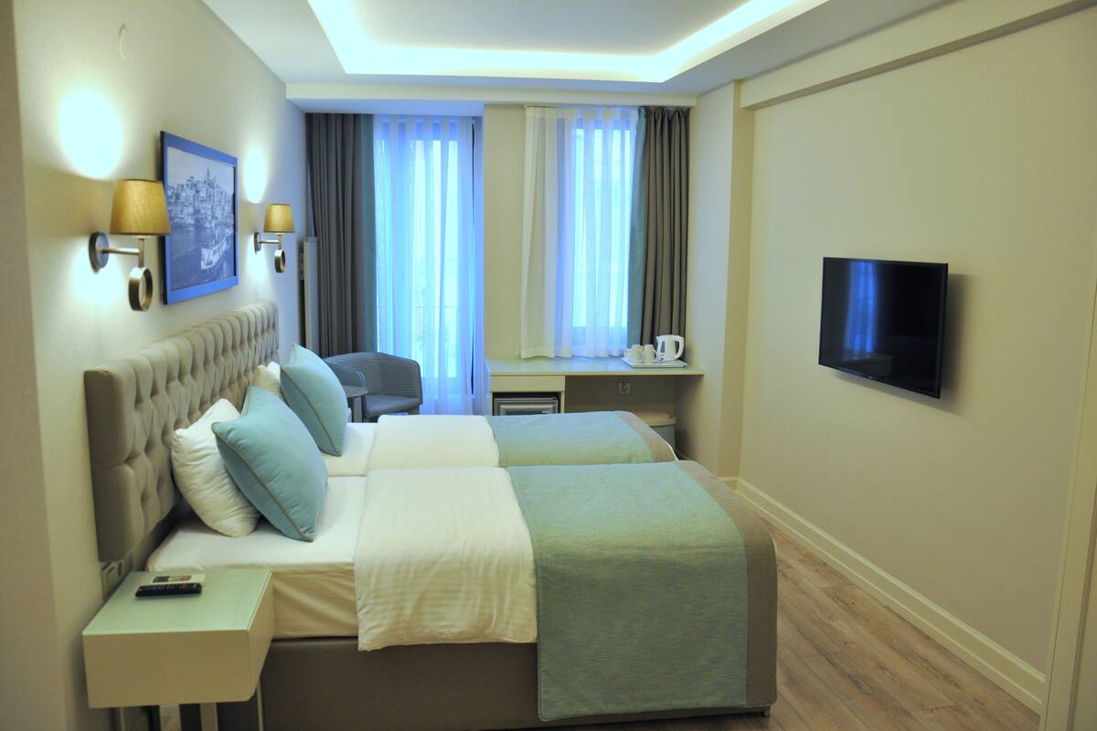 A hotel room with two beds, a television, a desk with a chair, and a window with curtains.