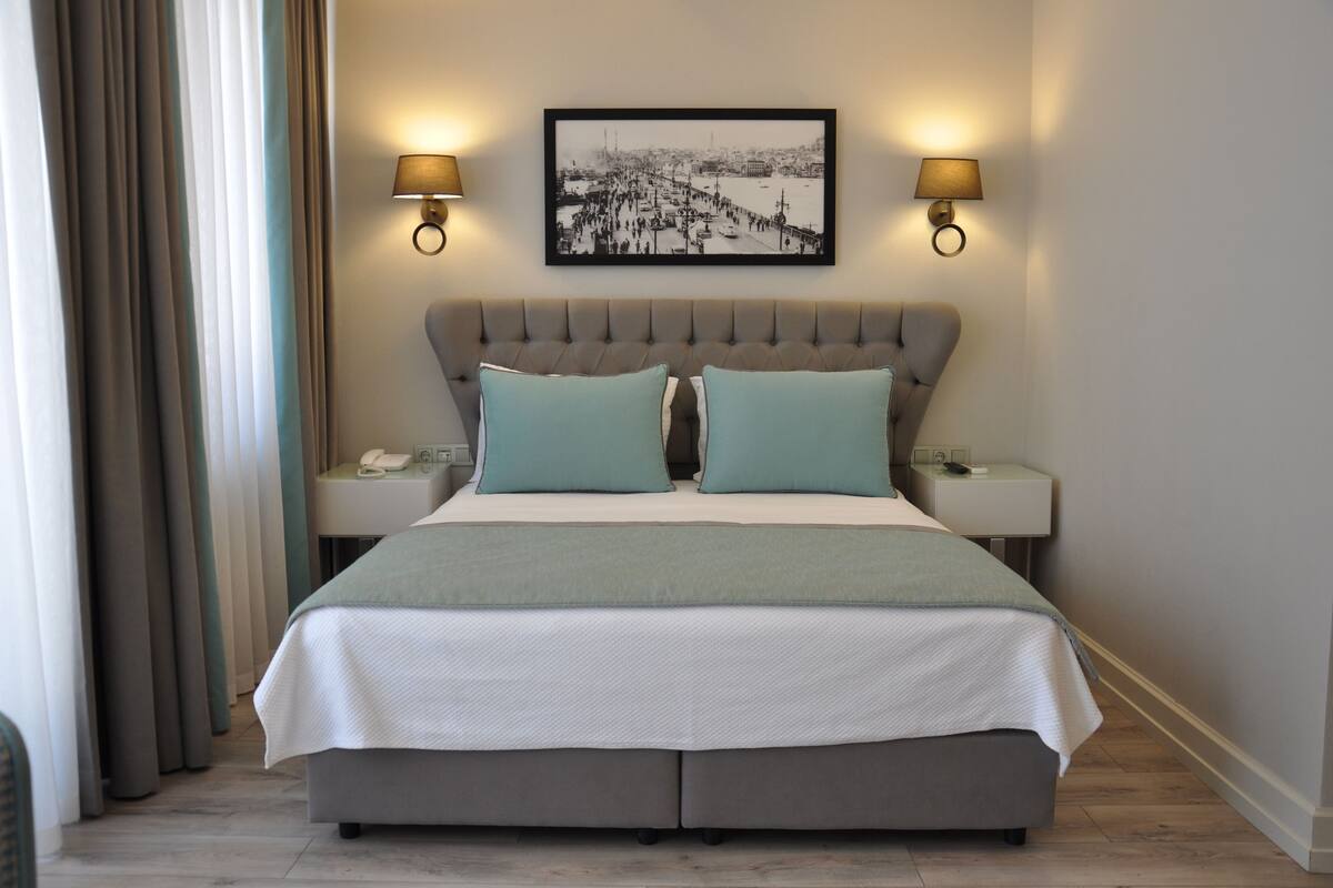 A hotel room with a large bed, two bedside tables, a nightstand, a framed picture on the wall, and two wall-mounted lamps.